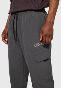 Grijze cargobroek met een taillekoord, zijzakken en geborduurd "HALO 1968/1972"-detail op het bovenbeen. Glad, lichtgewicht materiaal.