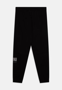 Pantalons de survêtement noirs en tissu doux. Dotés d'une taille élastique et d'un petit logo graphique sur la jambe inférieure gauche.