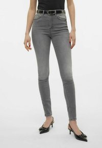 Jeans ajustados de talle alto en gris con cinco bolsillos y trabillas para cinturón, combinados con tacones negros tipo slingback con un detalle de lazo en la punta.