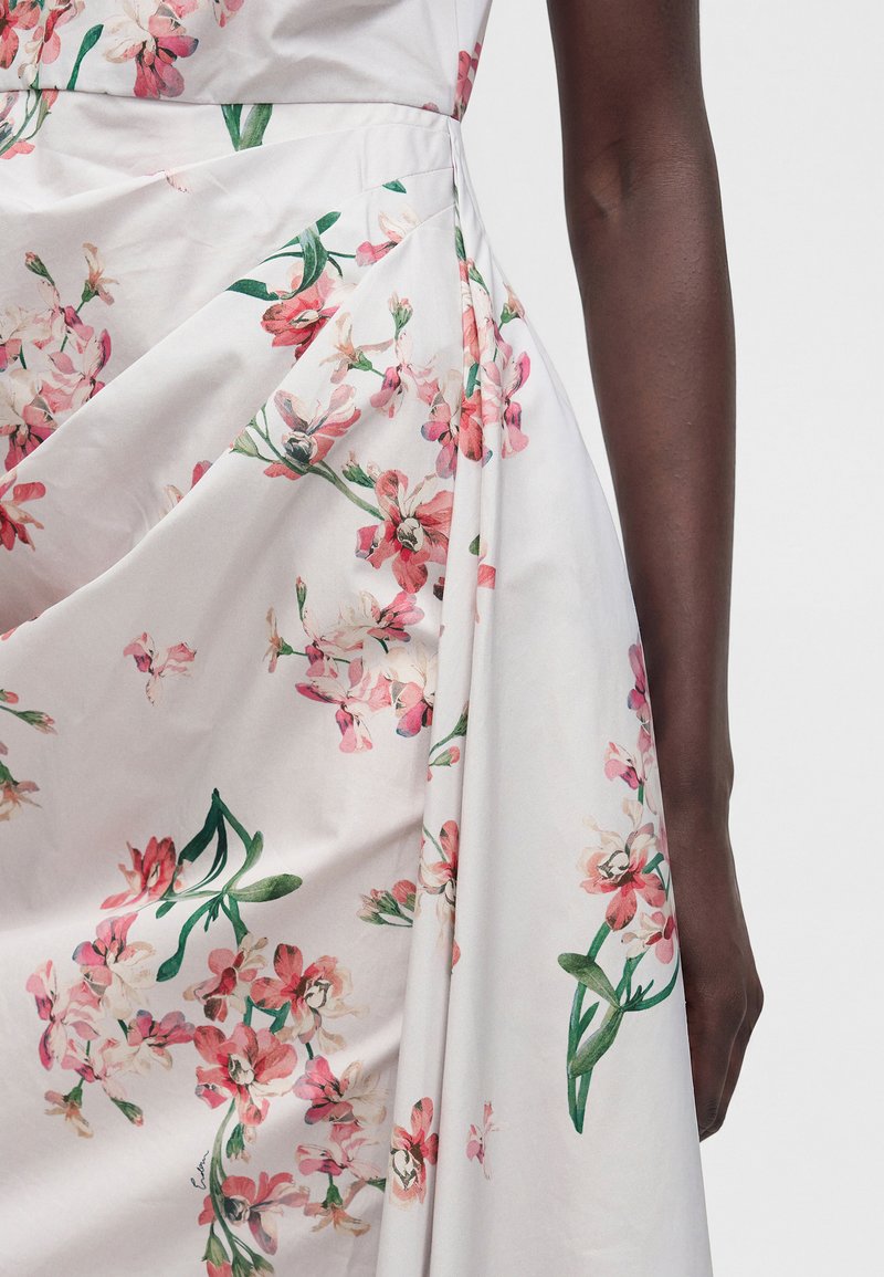White fabric with pink and green floral pattern draped and pleated around a dark-skinned arm, showcasing dress detail and texture.