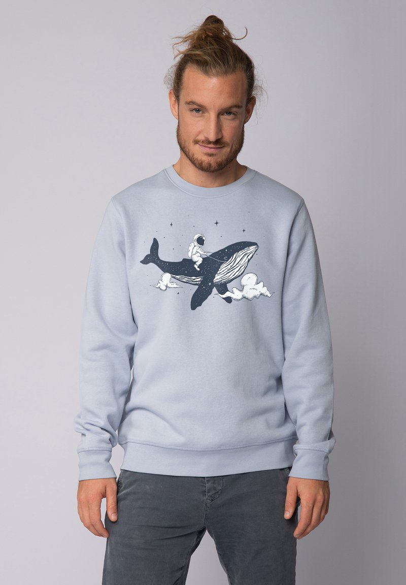 Sweatshirt bleu clair en tissu doux, présentant un graphisme d'un astronaute chevauchant une baleine sur fond étoilé.