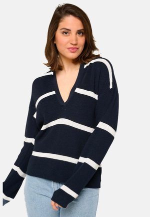 Pull marin avec des rayures horizontales blanches, design en V, texture côtelée et manches longues, associé à un jean en denim clair.