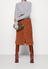 Šedý pletený svetr, oranžová manšestrová sukně s předním rozparkem a hnědé kozačky sahající nad kolena. Malá olivově zelená kabelka se stříbrným kováním.