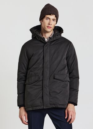 Dunkle Steppjacke mit Kapuze, ausgestattet mit einem Frontreißverschluss, zwei großen Fronttaschen und einer glatten, matten Oberfläche. Kombiniert mit einer gestrickten Mütze.