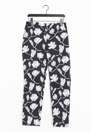 Sorte bukser med hvidt mønster af blomstergrene hængende på sort bøjle mod hvid baggrund.