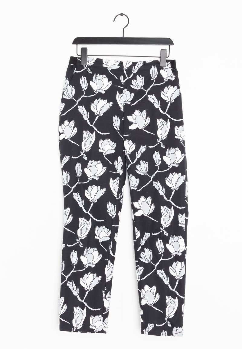 Pantalon noir avec motif de branche florale blanche suspendu sur un cintre noir contre un fond blanc.