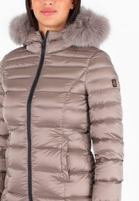Giacca puffa color taupe con design a righe orizzontali, chiusura con zip, tasche laterali e bordo del cappuccio in pelliccia grigia rimovibile.