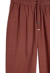 Rdzawoczerwone, miękkie spodnie z elastycznym pasem, sznurkiem do ściągania oraz bocznymi kieszeniami z gładkim srebrnym akcentem.