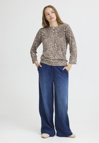 Leopardenmuster Langarmoberteil in braunen Farbtönen, kombiniert mit lockeren blauen Jeans. Weicher Stoff und weit geschnittenes Design. Helle beige Schuhe.