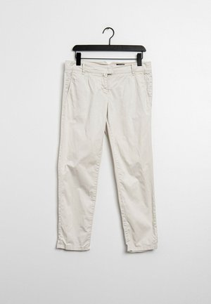 Pantalon décontracté beige clair suspendu sur un cintre noir devant un mur blanc uni.