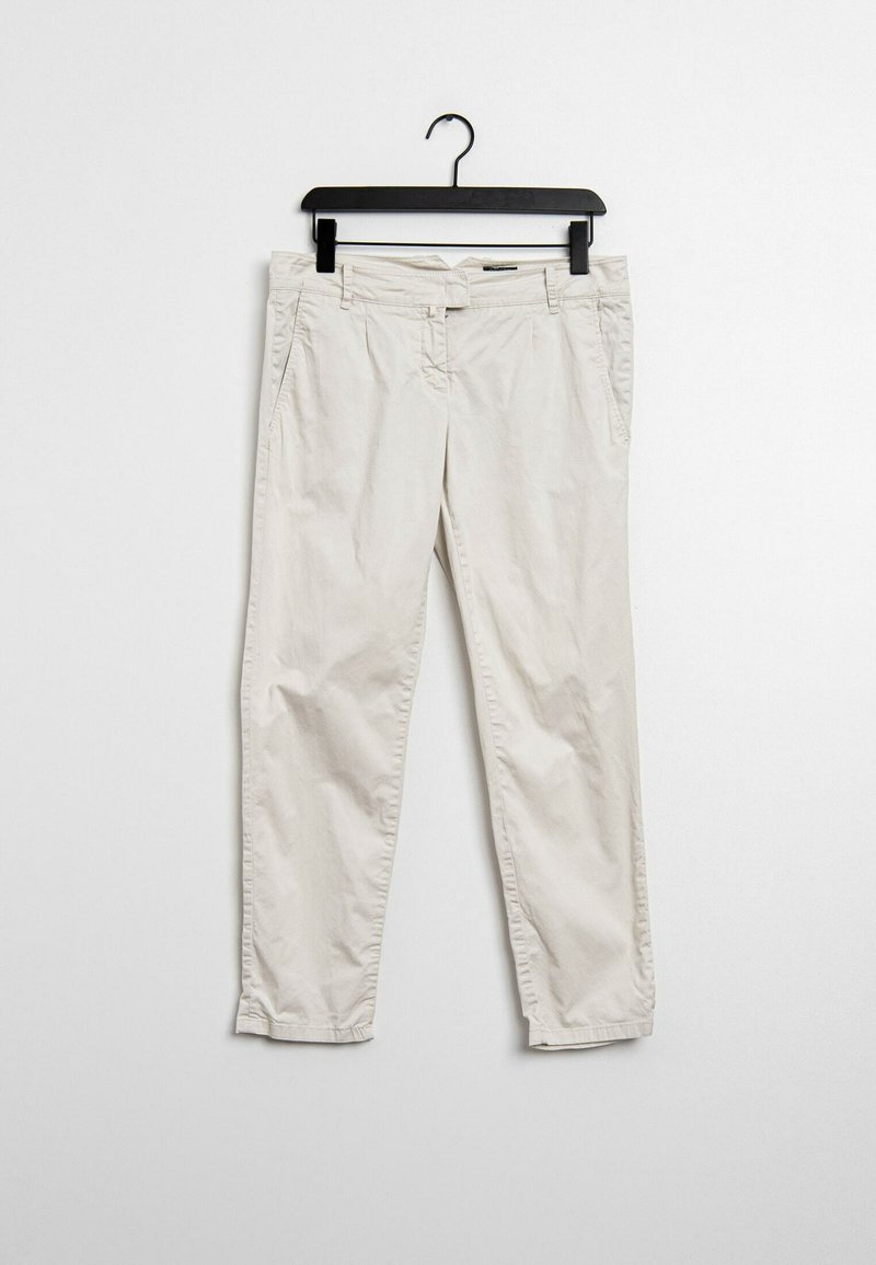 Pantalon décontracté beige clair suspendu sur un cintre noir devant un mur blanc uni.