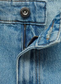 Jeans din denim de culoare albastru deschis cu cusături în contrast, prezentând un sistem de închidere cu buton metalic și un fermoar. Perspectivă detaliată asupra texturii materialului.