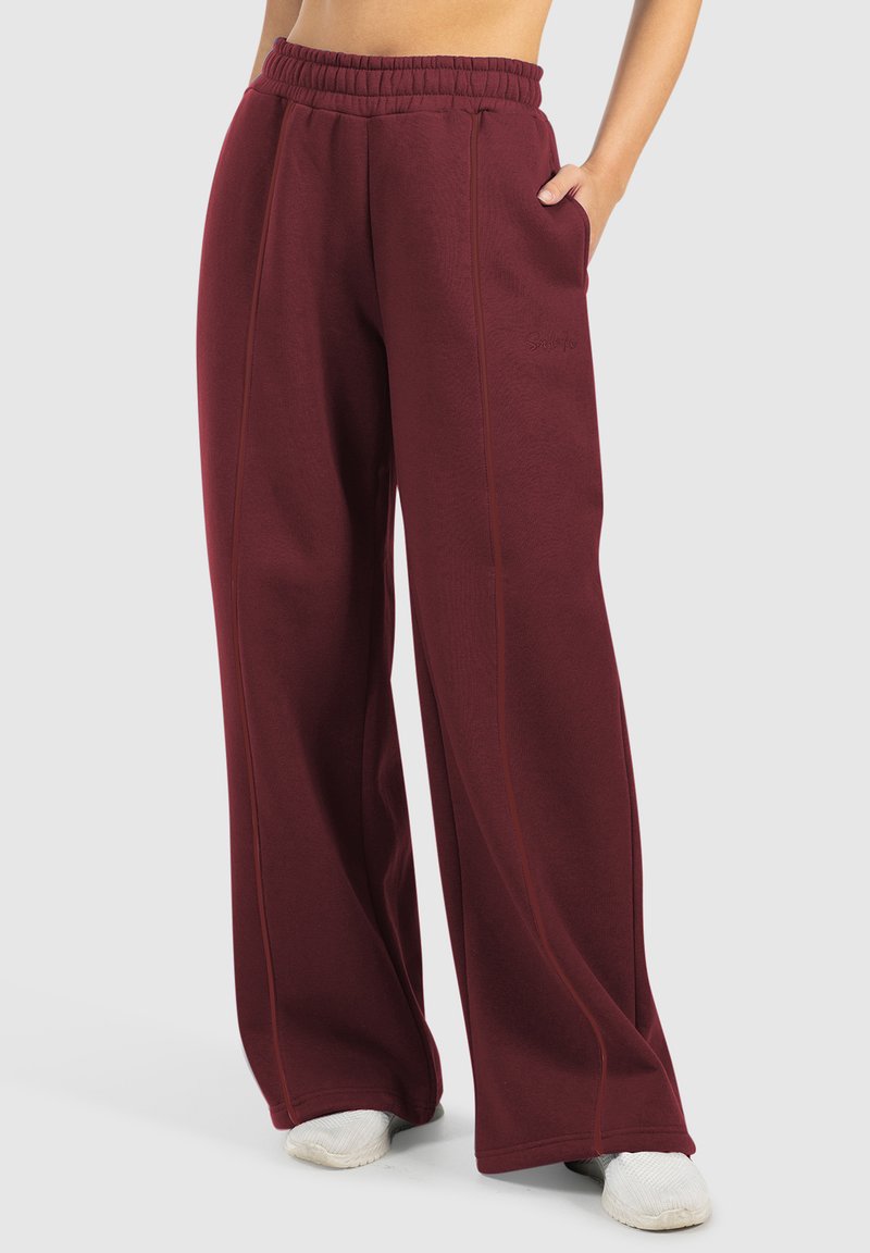 Bordeaux kleurige sweatpants met wijde pijpen, een elastische tailleband, zijzakken en contrasterende stiksels. Soepele textuur, casual ontwerp.