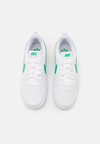 White sneaker with green accents, featuring a smooth leather upper, perforated toe box, and flat laces. Nike logo on tongue and side.