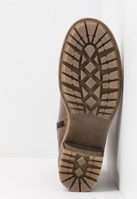 Botte marron avec une semelle en caoutchouc texturée, présentant un motif de bande de roulement en zigzag. Détail de fermeture éclair latérale et taille indiquée comme 37.