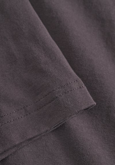 Tessuto di cotone in una tonalità di viola tenue, con una texture liscia, cuciture visibili lungo l'orlo e una trama del tessuto sottile.