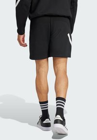 Pantaloni sportivi neri con una finitura testurizzata, con un dettaglio del logo bianco. Abbinati a calze a righe bianche e nere e scarpe Adidas.
