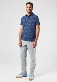 Camisa de manga corta azul marina con un estampado floral, pantalones a rayas gris claro y zapatillas azul y plata con detalles de cordones.