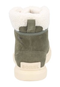 Bota de invierno de ante verde oliva con forro de felpa blanca, suela beige, tira de agarre y marca "SOREL" en el talón.