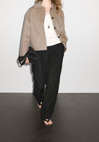 Beige uldblandet cropped jakke med sorte knapper, hvid tank top, sorte plisserede wide-leg bukser og sorte vævede håndtaske.