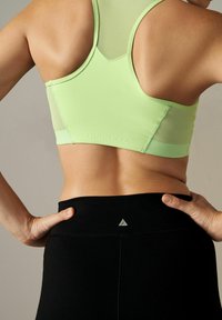 Light green sports bra with mesh detail, featuring a subtle logo, paired with high-waisted black leggings displaying a small logo at the waistband.