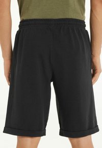 Černé bavlněné šortky s elastickým pasem, do délky kolen, s ohrnutými manžetami a hladkým povrchem. Jednoduchý design bez vzorů.