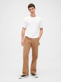 Λευκό μπλουζάκι με κοντά μανίκια συνδυασμένο με καφέ παντελόνι ίσιας γραμμής. Η εμφάνιση ολοκληρώνεται με μαύρα και λευκά πάνινα sneakers, παρουσιάζοντας ένα casual στυλ.