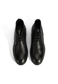 Chaussures en cuir noir avec une finition texturée, présentant un bout rond et trois œillets pour les lacets. Accents lisses et mates sur la tige.