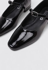 Zapatos Mary Jane de charol negro con punta cuadrada, con una correa en el tobillo con hebilla plateada y forro interior suave.