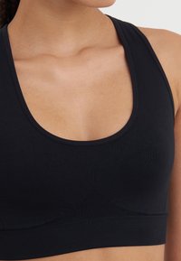 Black sports bra with a scoop neckline, made from smooth fabric. Features a ribbed band at the bottom and seamless design for comfort.