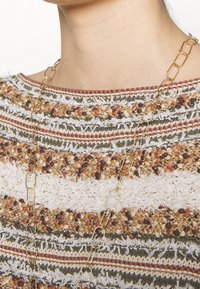 Beige und mehrfarbiger gestreifter Pullover mit unterschiedlichen Garnen, ausgestattet mit goldfarbenen Ketten-Details am Hals.