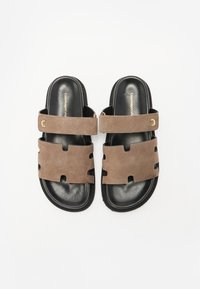 Brune semskede slidesandaler med sorte gummisåler, der har to brede stropper med udskæringer og guldhardware.