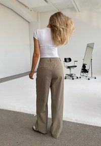 Beige high-waisted trousers with a wide-leg cut, paired with a fitted white shirt. Smooth fabric and minimalistic design.