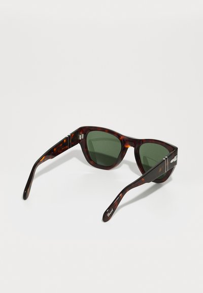 Óculos de sol em padrão tartaruga com lentes verdes. Design de armação quadrada, acabamento brilhante, detalhes em metal nas hastes e braços esguios.