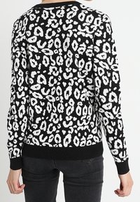 Svart tröja med ett vitt abstrakt leopardmönster, ribbade ärmar och nederkant. Texturen ser ut att vara stickad med en mjuk finish.