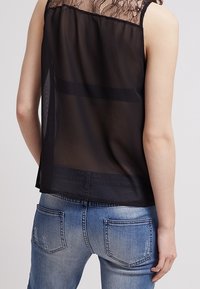 Sort gennemsigtig ærmeløs top med en blondekant, parret med lyseblå slidte jeans med baglommer og en falmet tekstur.