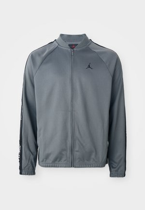 Siva sportska jakna na raszip s crnim bočnim trakama i malim crnim Jumpman logom na lijevoj strani prsnog koša.