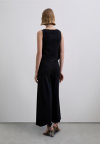 Top negro sin mangas con dobladillo curvado combinado con pantalones de pierna ancha. El conjunto presenta una textura sutil y sandalias de tacón alto con estampado de serpiente.