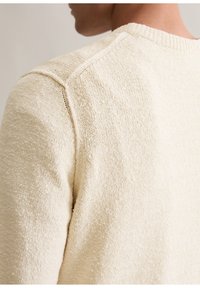 Strickpullover in Creme mit strukturierter Oberfläche, geripptem Rundhalsausschnitt und eingesetzten Schulternähten, aus sanftem, leichtem Material.