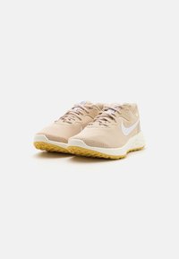 Par de zapatillas de running Nike color beige con logotipos Swoosh blancos y suelas color goma, exhibidas sobre un fondo blanco.