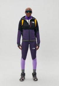 Ytelsesteknisk friluftsjakke i svart og lilla. Kombinert med lilla tights, grå sokker og fjellsko. Inkluderer også en ryggsekk og solbriller.