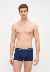 Marineblaue Boxershorts aus weichem Material mit einem elastischen, gebrandeten Bund. Das Modell steht oberkörperfrei da und präsentiert einen modernen, figurschmeichelnden Schnitt.