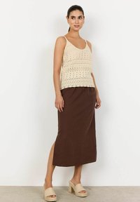 Top in maglia beige con motivo a traforo, abbinato a una gonna marrone lunga fino alla caviglia con uno spacco laterale. Sandali con tacco a blocco intrecciato.