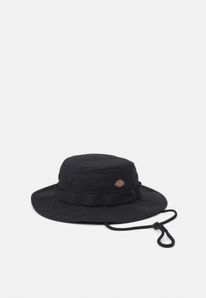 Sort hat med bred skygge og justerbar hagesnor samt lille rund logo-patch foran på en ensfarvet hvid baggrund.