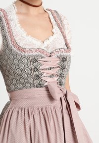 Vêtement traditionnel avec un corsage gris à motifs, un laçage en ruban rose, un col en dentelle blanche et une jupe rose à pois avec une taille nouée.