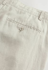 Pantaloni in lino grigio chiaro con tasca posteriore dotata di chiusura a bottone singolo e un motivo testurizzato sottile.