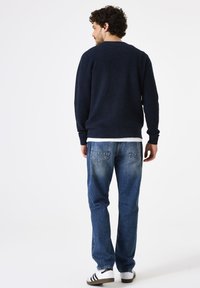 Marineblauwe waffle-knit trui, relaxed fit, gecombineerd met lichtblauwe jeans en witte sneakers met zwarte strepen. Zichtbare stiksels en zakken op de jeans.