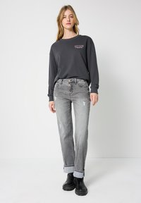 Szara bluza z napisem "GUYS CLUB", zestawiona z jasnoszarymi dżinsami z przetarciami, złożonymi mankietami i czarnymi, masywnymi butami. Prosty, casualowy styl.