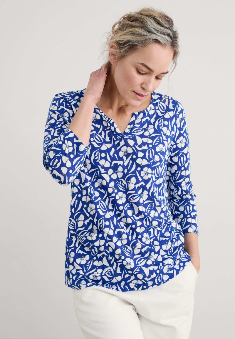 Blusenshirt mit blauem Muster und floralem Design in Weiß, aus weichem Stoff gefertigt, mit Dreiviertelärmeln und V-Ausschnitt.