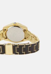 Orologio dorato con cassa ottagonale, bracciale in acciaio inossidabile con accenti neri e finitura liscia e lucida sul retro.